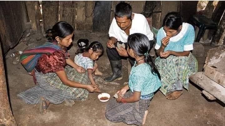 Eine Familie sitzt auf dem Boden und teilt sich das Essen. In einer schwach beleuchteten Wohnung. 
