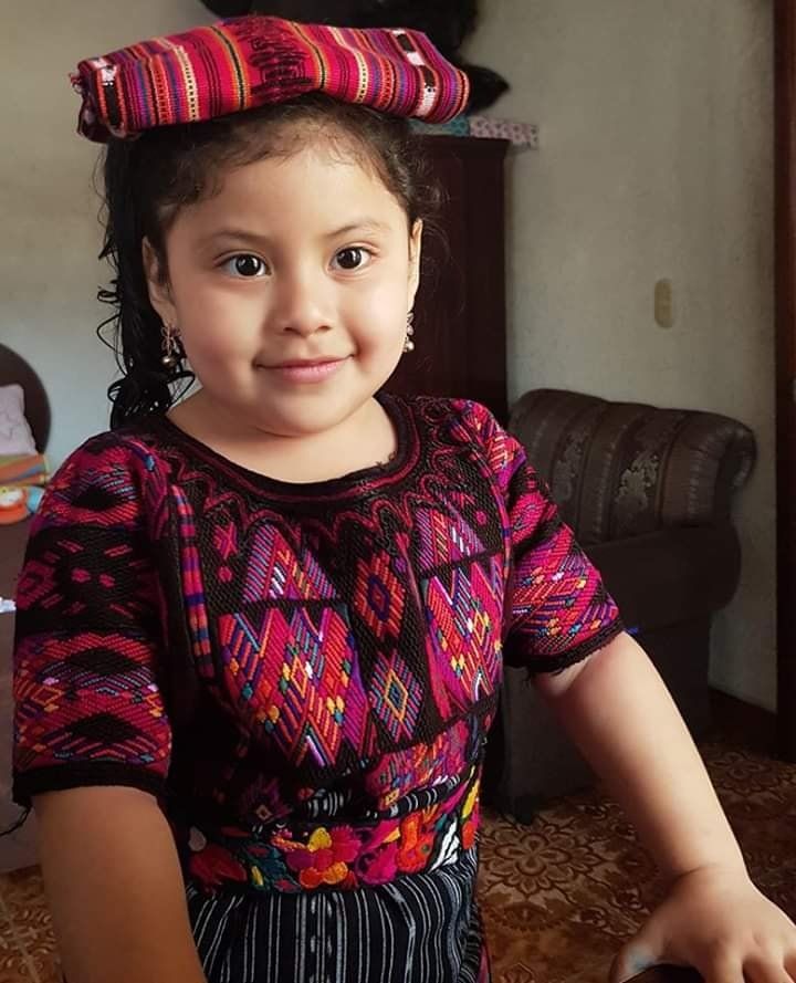 Mädchen in traditioneller guatemaltekischer Kleidung lächelt in einem Innenraum.