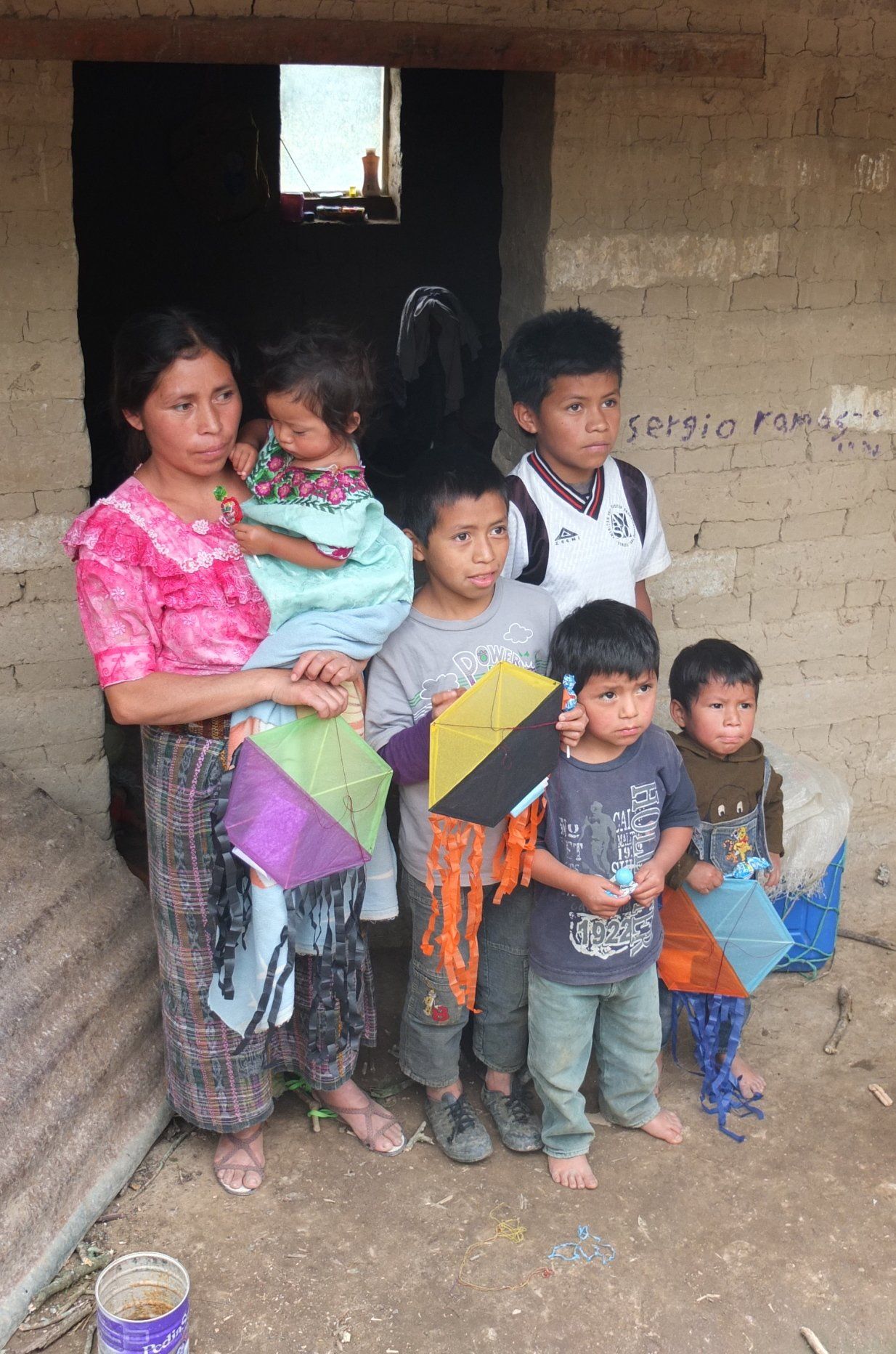 Eine Frau und sechs Kinder posieren mit Drachen vor einem Gebäude.