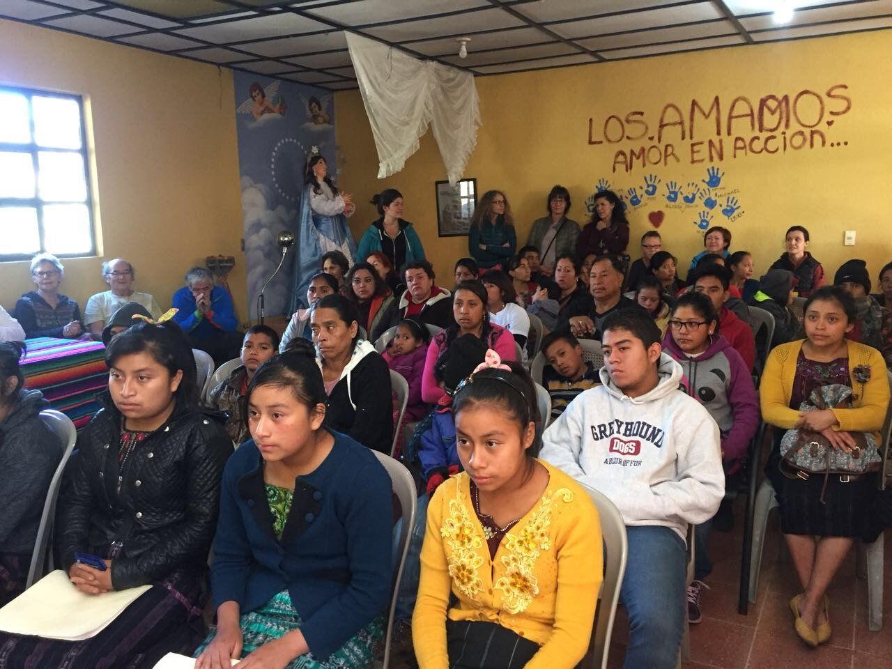 Menschen sitzen drinnen und hören zu; Gemälde von Maria; gelbe Wände; 