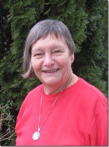 Frau in rotem Hemd lächelt im Freien inmitten von Grün, sie trägt einen Anhänger.