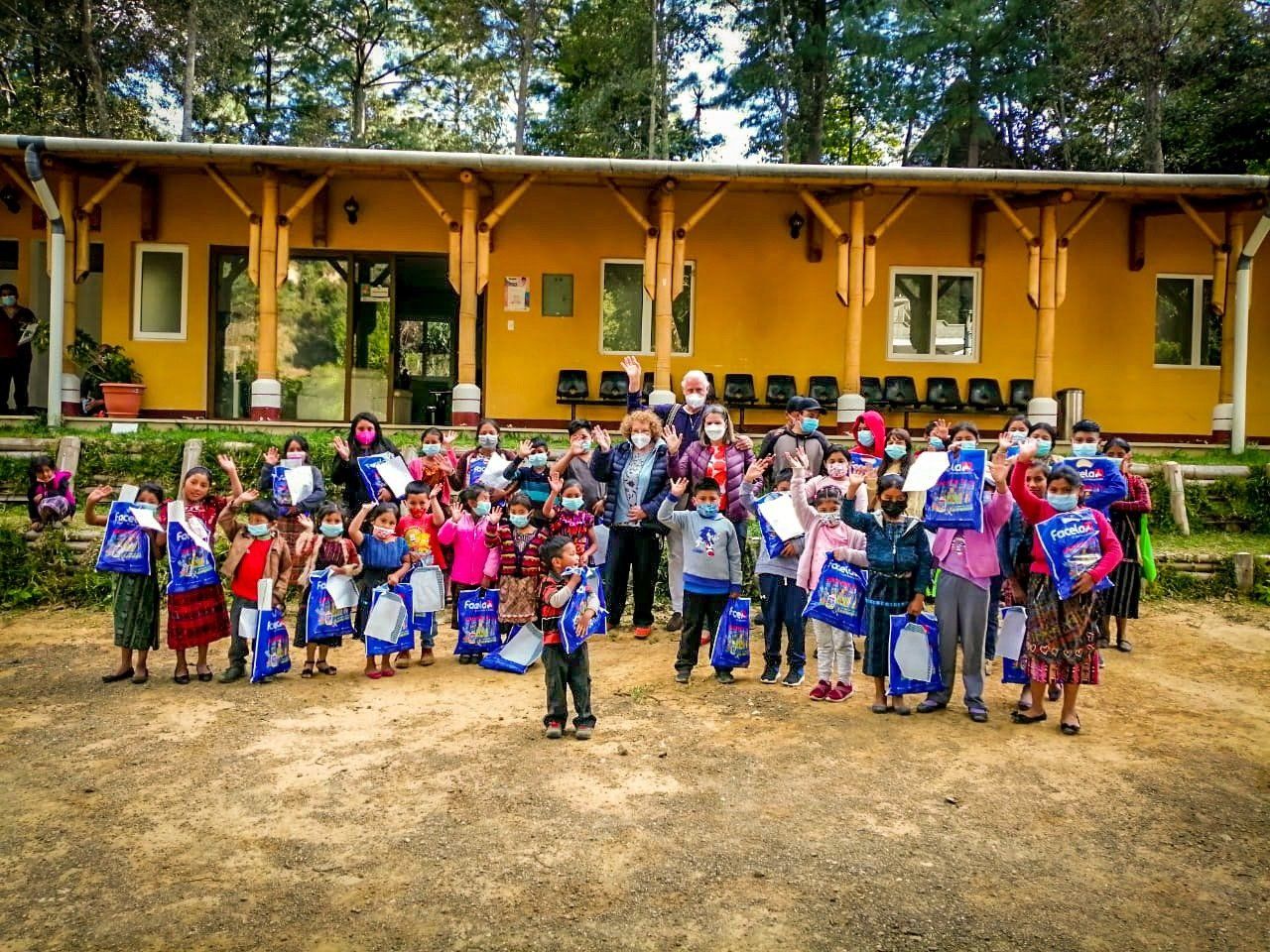 Eine Gruppe maskierter Kinder mit Taschen steht vor einem gelben Gebäude; im Freien.