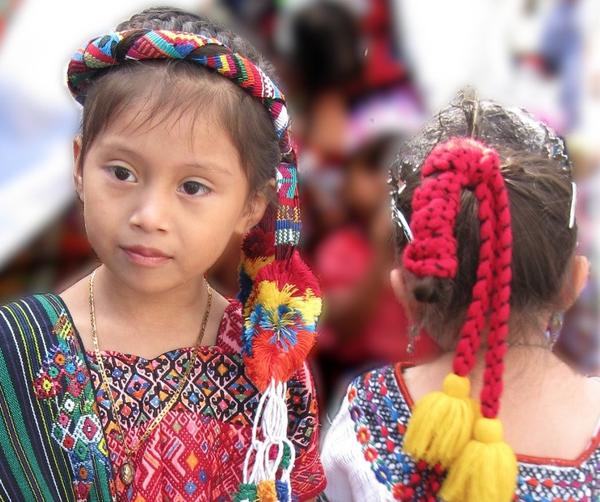 Zwei Mädchen in farbenfroher traditioneller guatemaltekischer Kleidung, eines schaut nach links.
