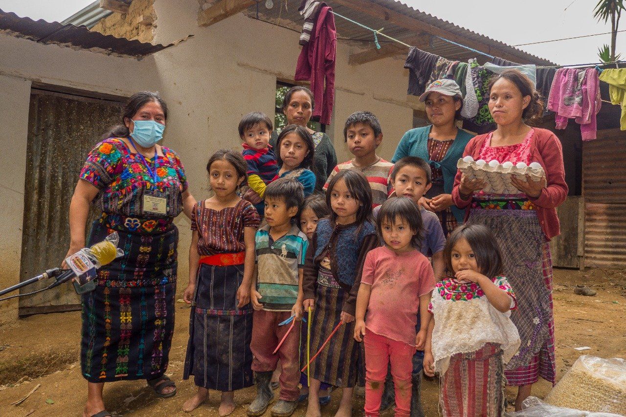 Eine Gruppe von Menschen, darunter auch Kinder, posiert vor einem Haus. Eine Frau hält Eier, eine andere trägt eine Maske.