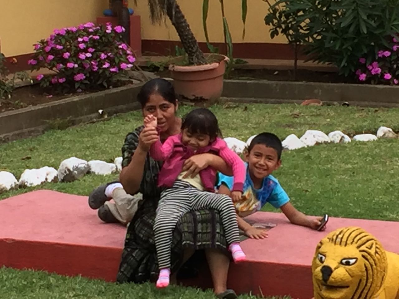 Frau sitzt mit zwei Kindern auf einer roten Bank; die Kinder lachen, eines sitzt auf dem Schoß der Frau; 