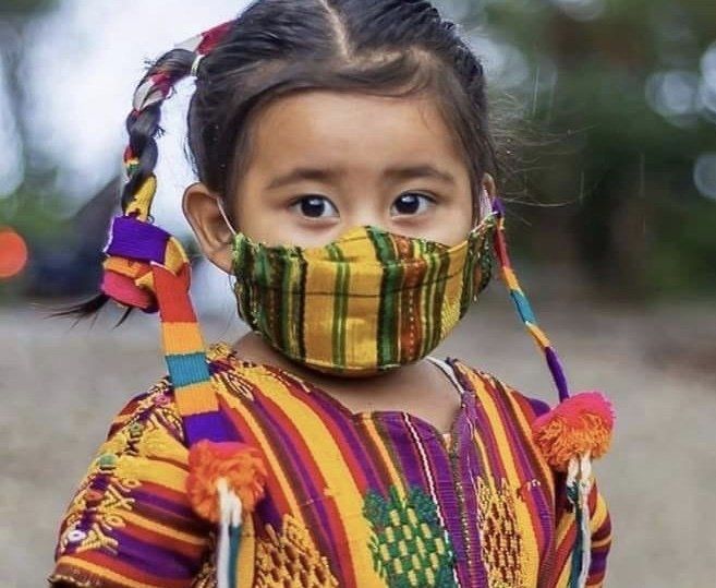 Mädchen in farbenfrohem, gewebtem Outfit und Maske, Zöpfe, im Freien.