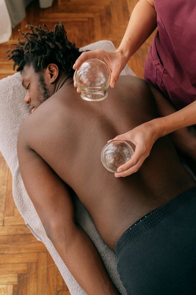 Man receiving cupping therapy on his back; therapist holds glass cups.