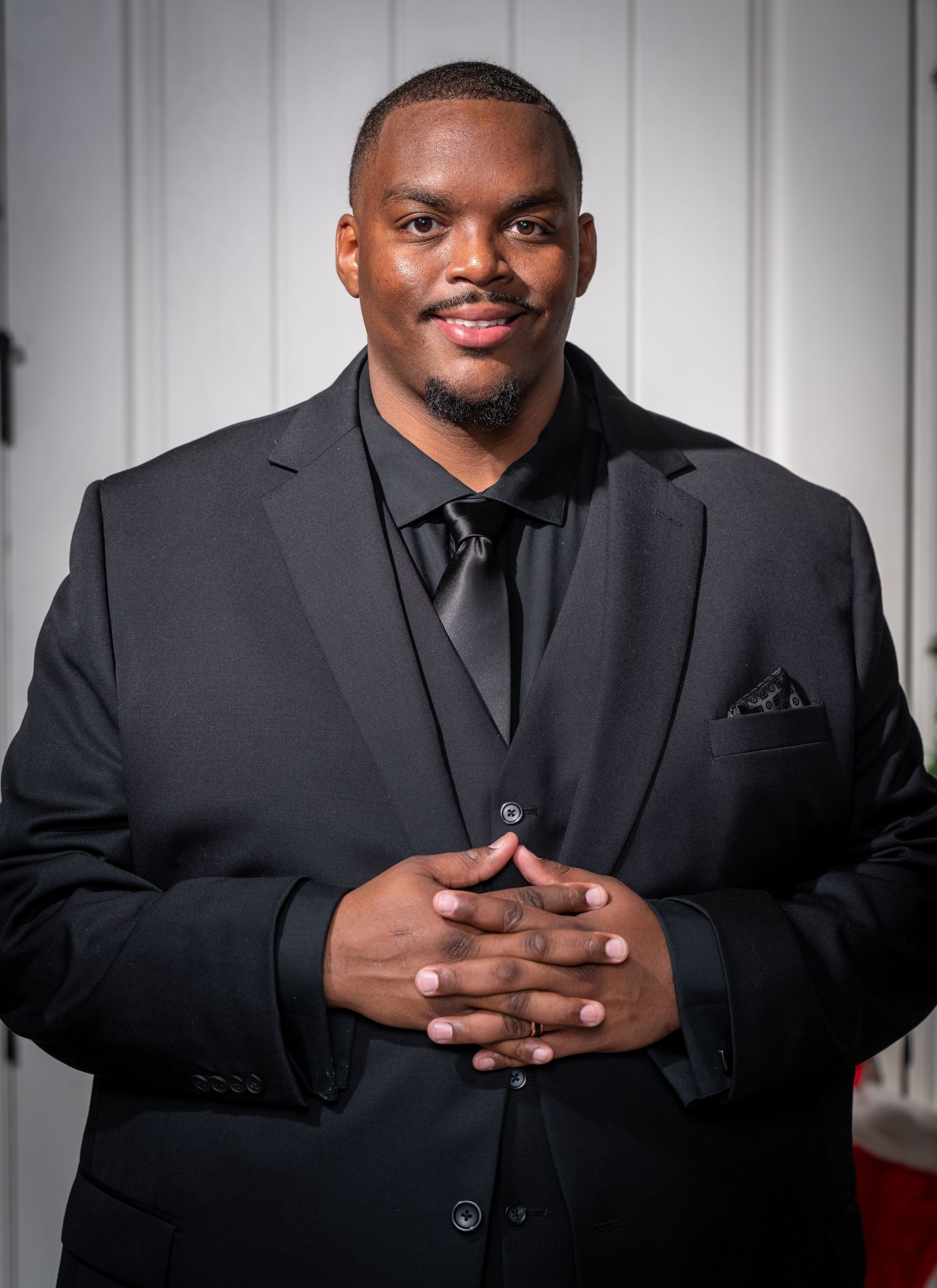 A man in a suit and tie is standing with his hands folded.