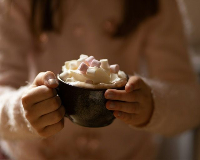 A woman is holding a cup of hot chocolate with whipped cream and marshmallows.