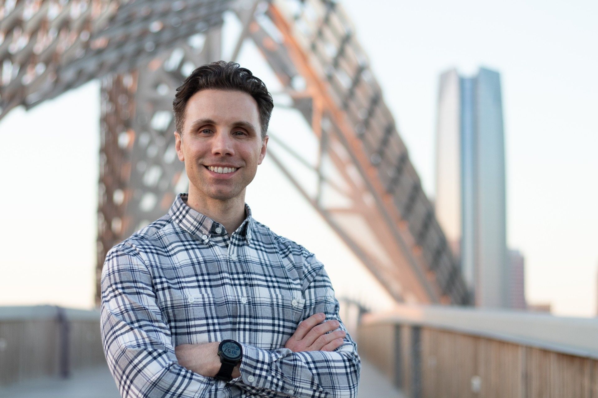 A man in a plaid shirt is standing on a bridge with his arms crossed.