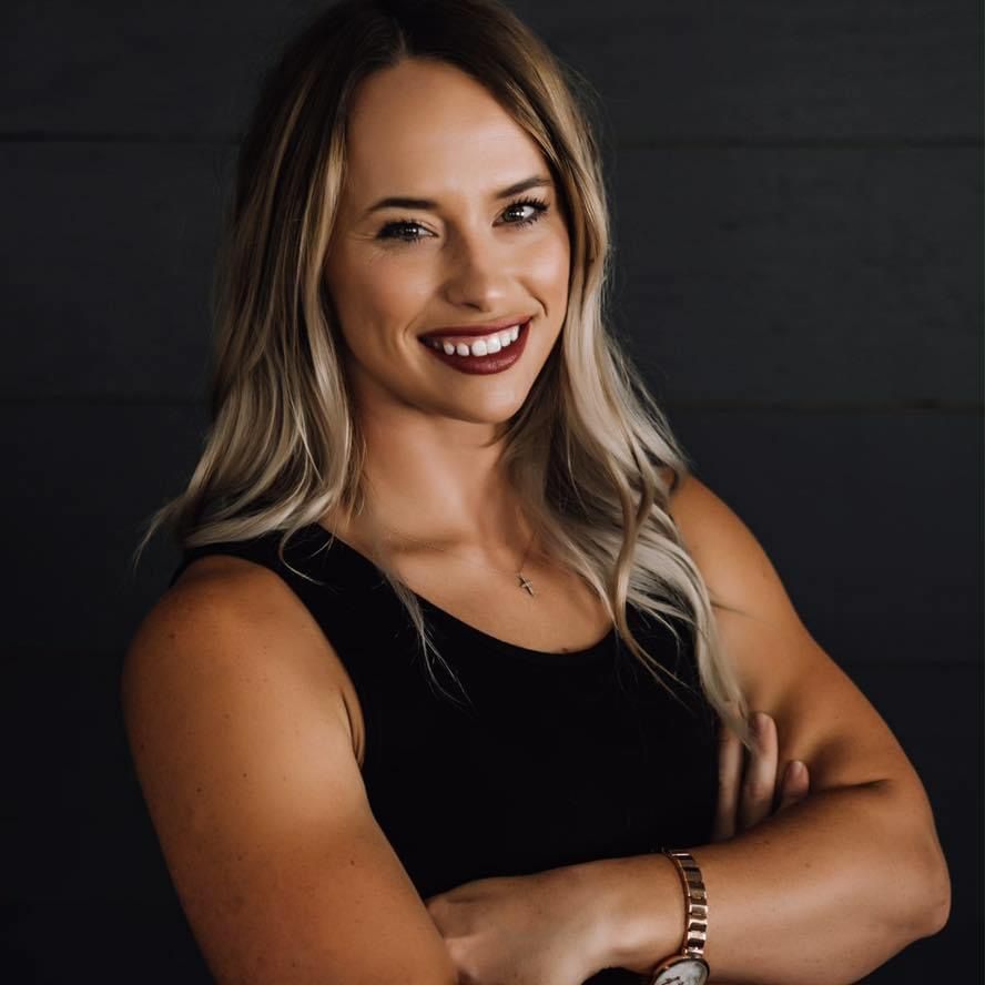 A woman in a black tank top is smiling with her arms crossed.