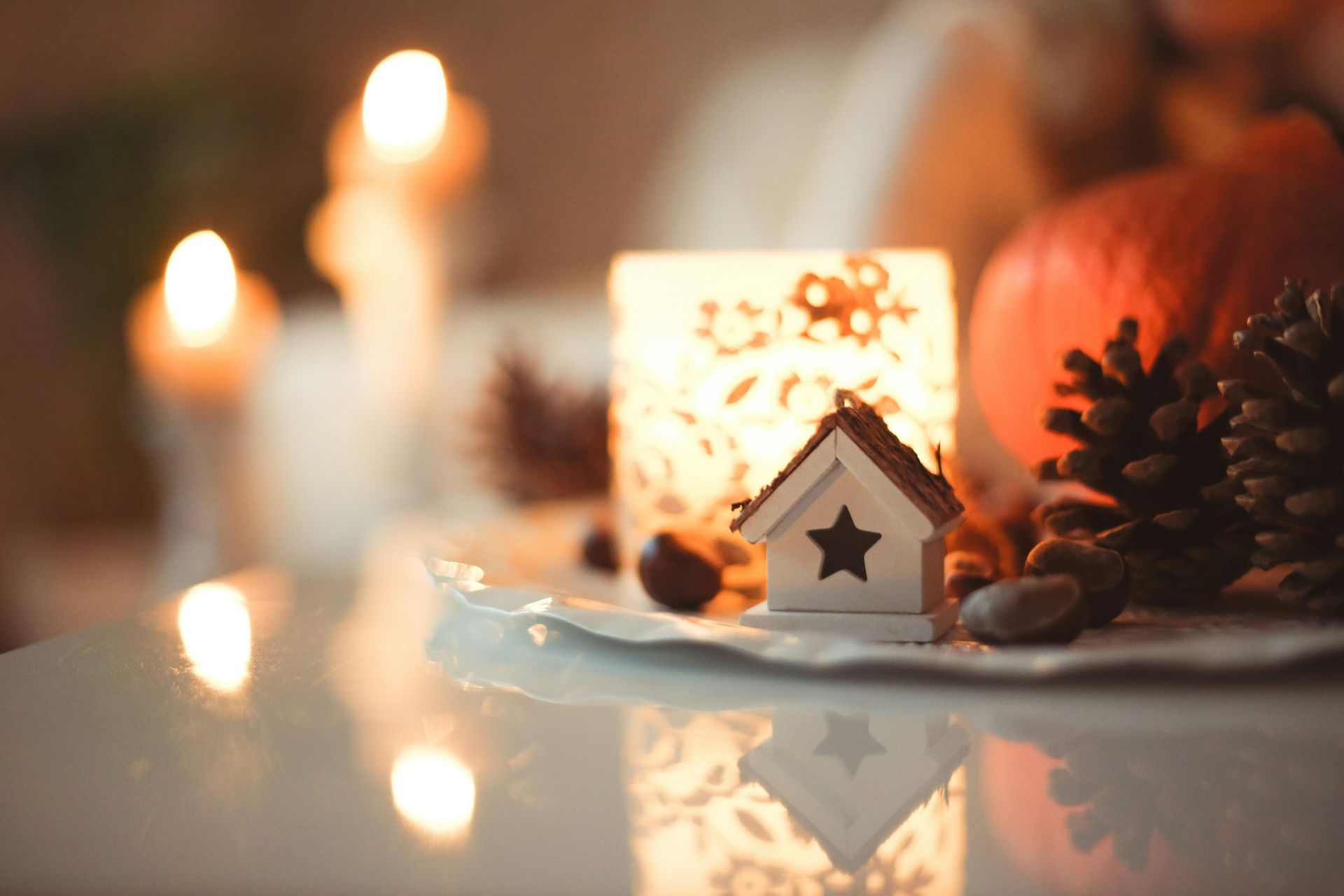 Close-up of a lit candle and decorative items including a small wooden house with star.