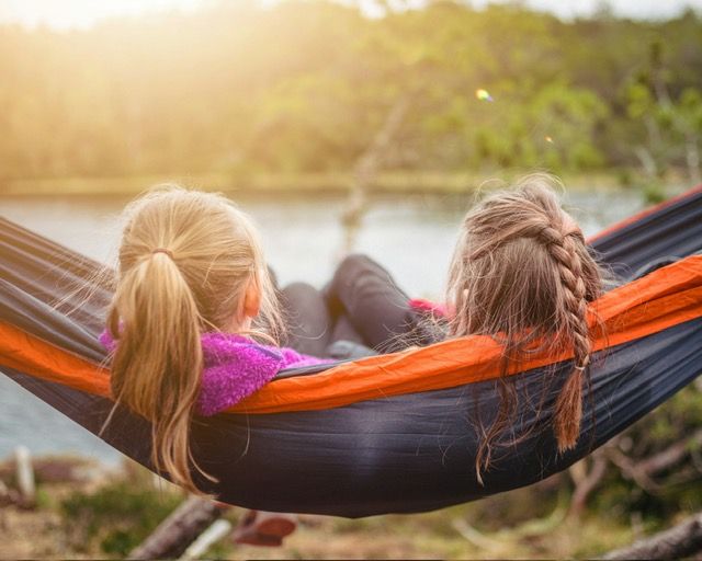 Two young girls are laying in a hammock near a lake.