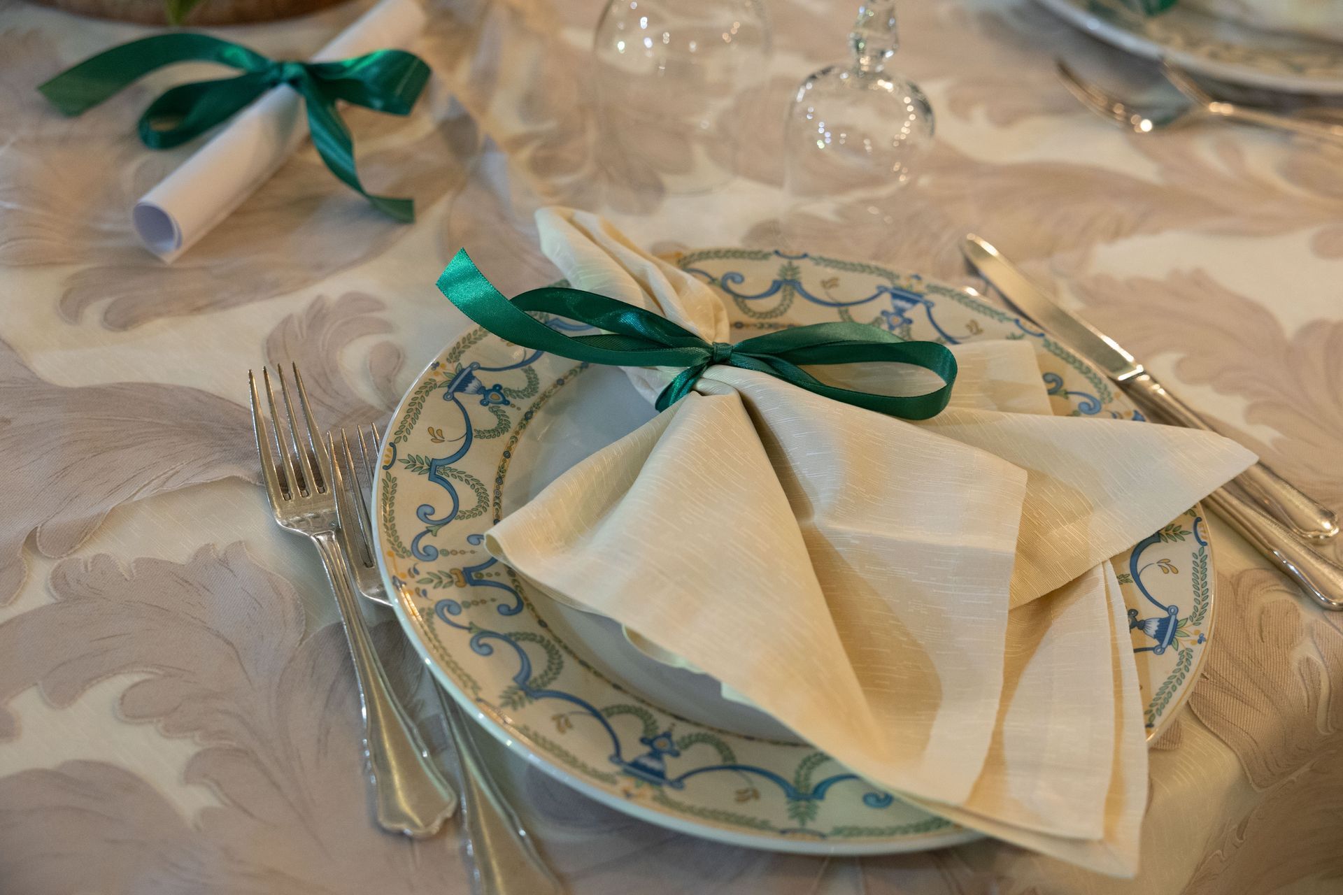 Apparecchiatura della tavola con piatto, tovagliolo legato con nastro verde, posate e pergamena.