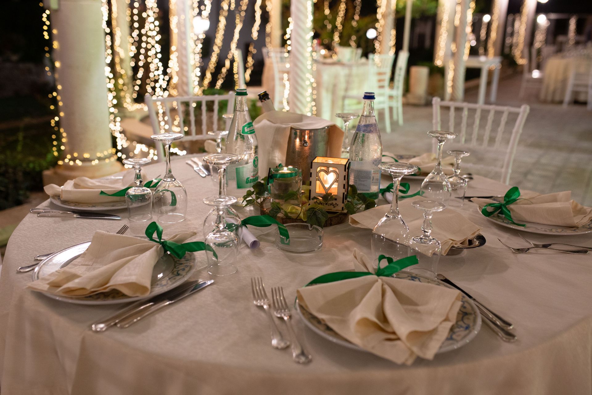 Tavolo da pranzo formale apparecchiato per un evento all'aperto con tovaglia bianca, posate e nastri verdi.