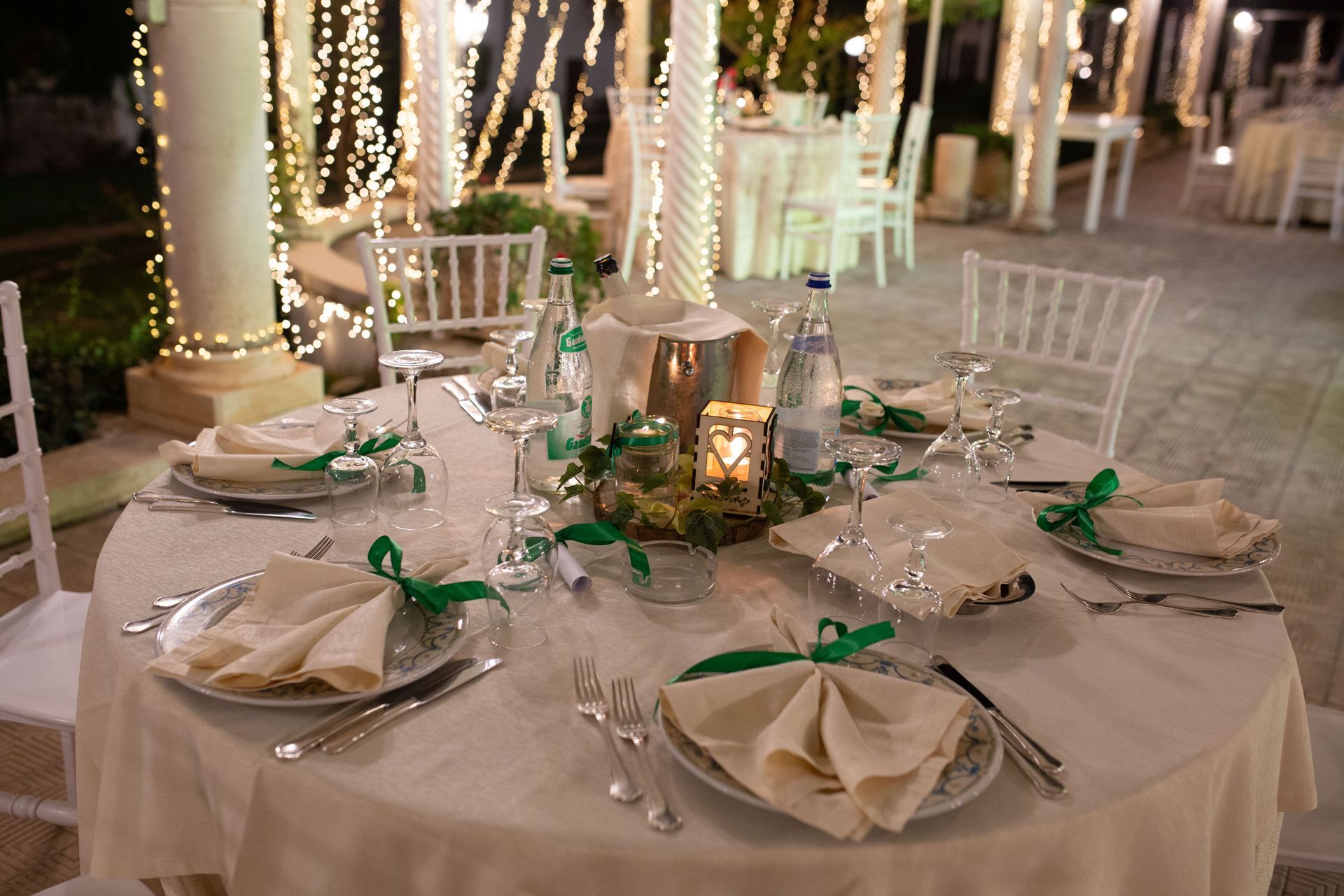 Elegante apparecchiatura per la tavola all'aperto con tovaglia bianca, piatti, posate e dettagli con nastro verde.