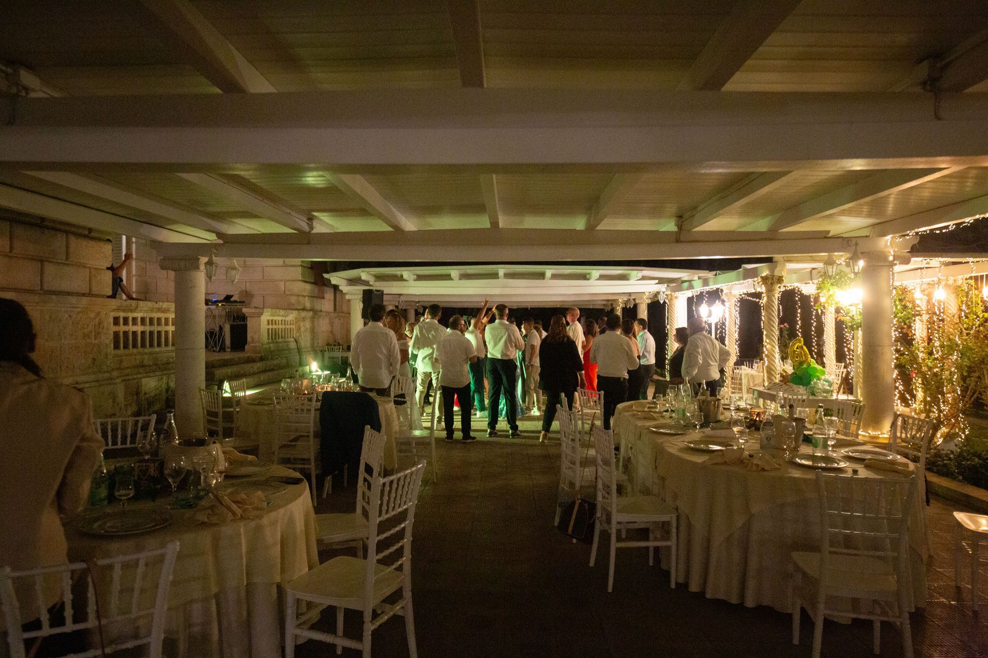 Festa all'aperto con tavoli apparecchiati per cenare e persone che ballano sotto un baldacchino illuminato.