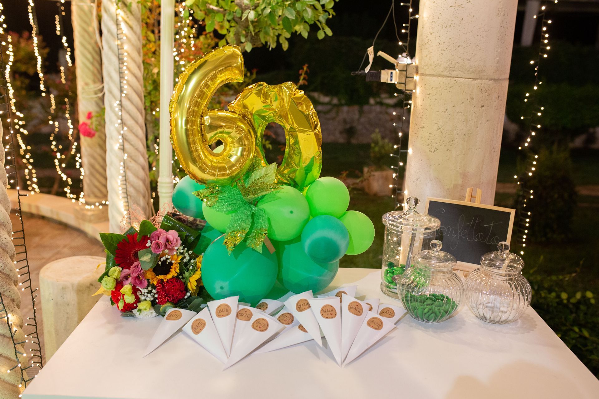 Un tavolo decorato per un 60° compleanno con palloncini, fiori e dolcetti.
