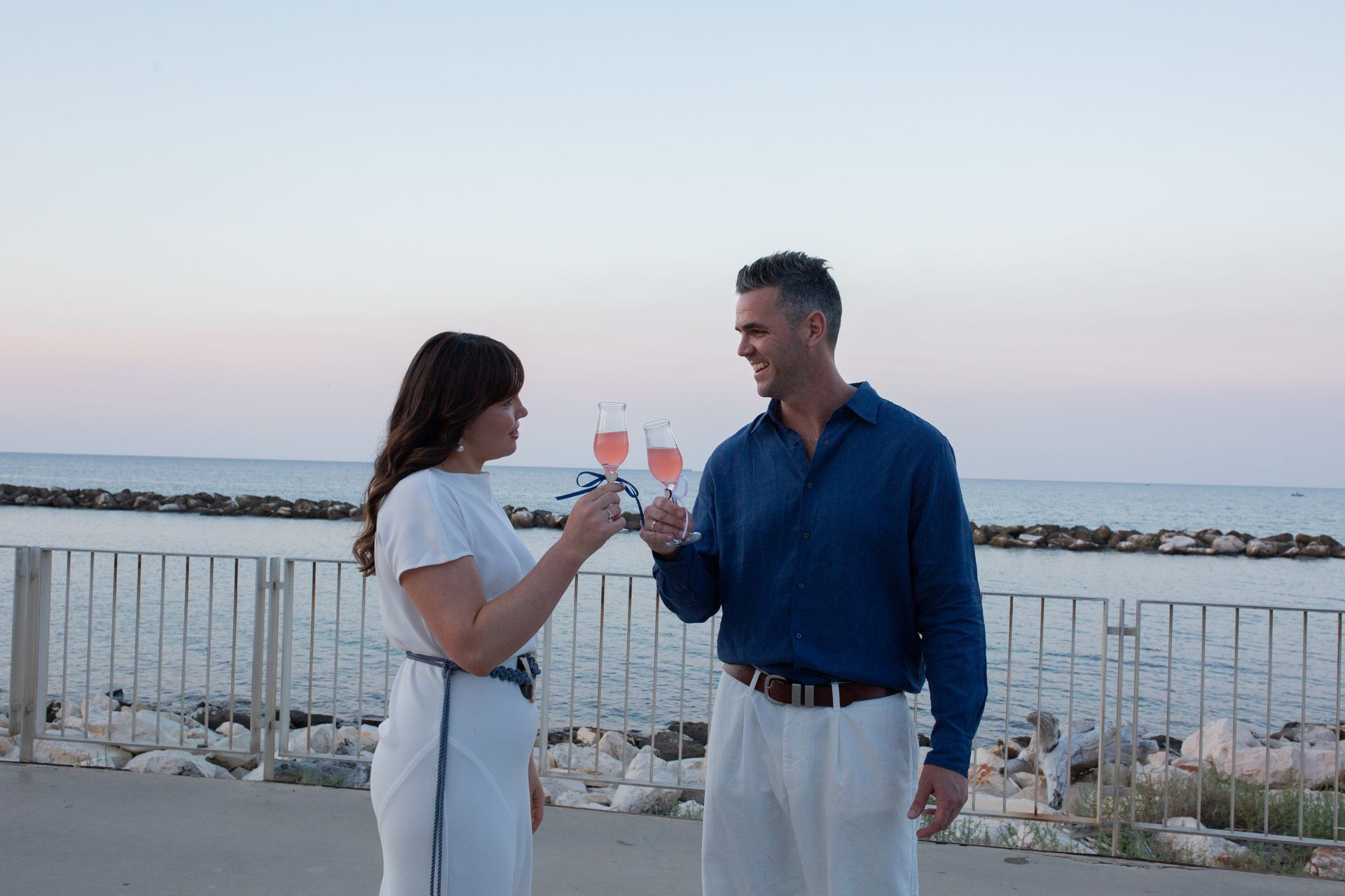 coppia di sposi che celebra il matrimonio brindando sul lungomare al tramonto