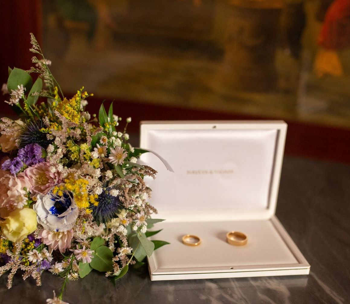 Bouquet da sposa accanto a una scatola portafedi contenente due fedi nuziali in oro.