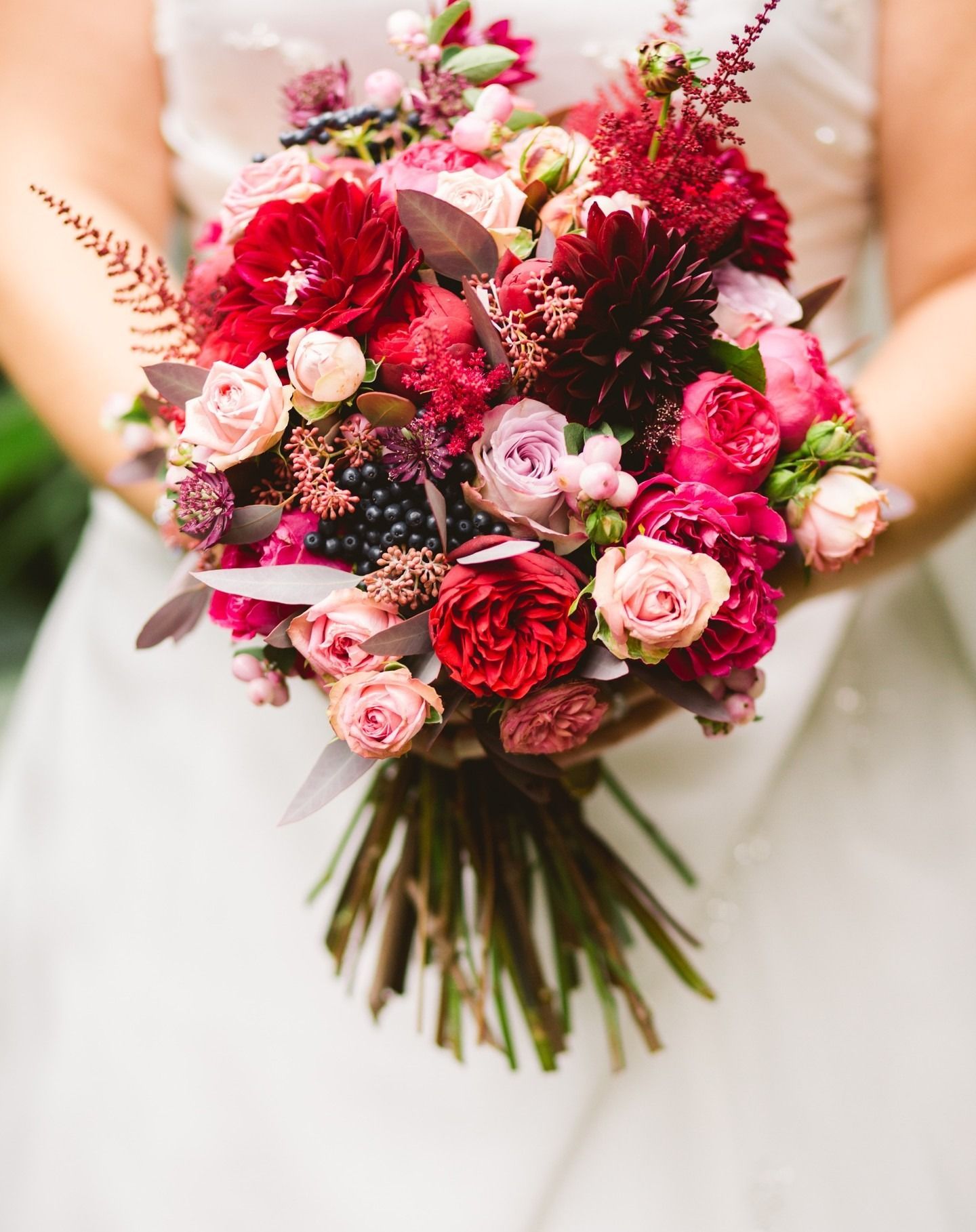 Sposa che tiene in mano un bouquet di fiori rossi e rosa, con verde.