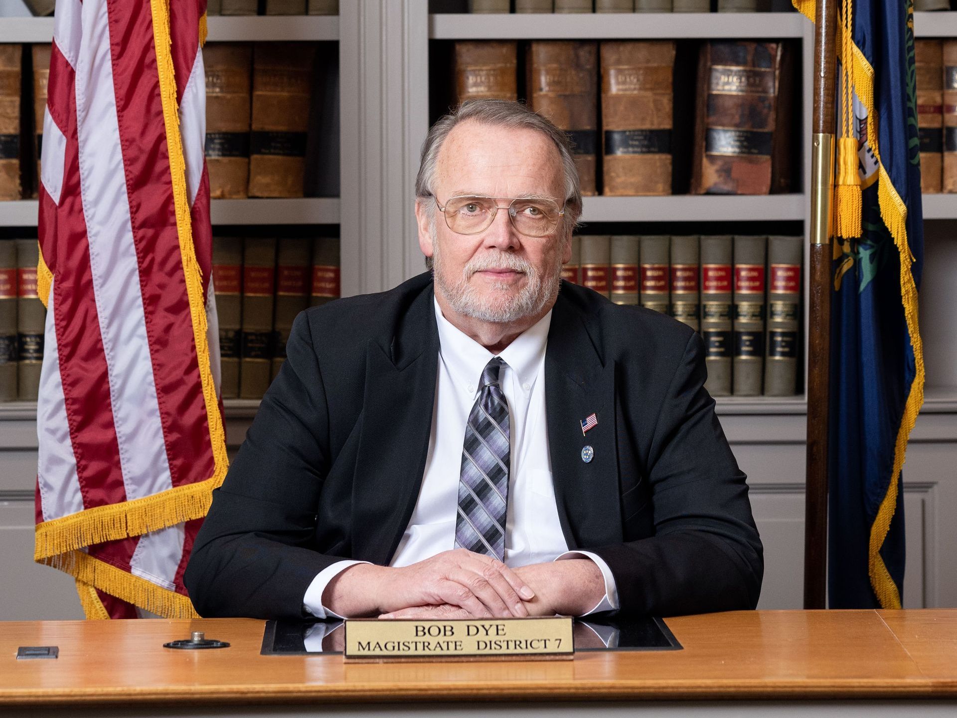 A man in a suit and tie is sitting at a desk in front of an american flag.