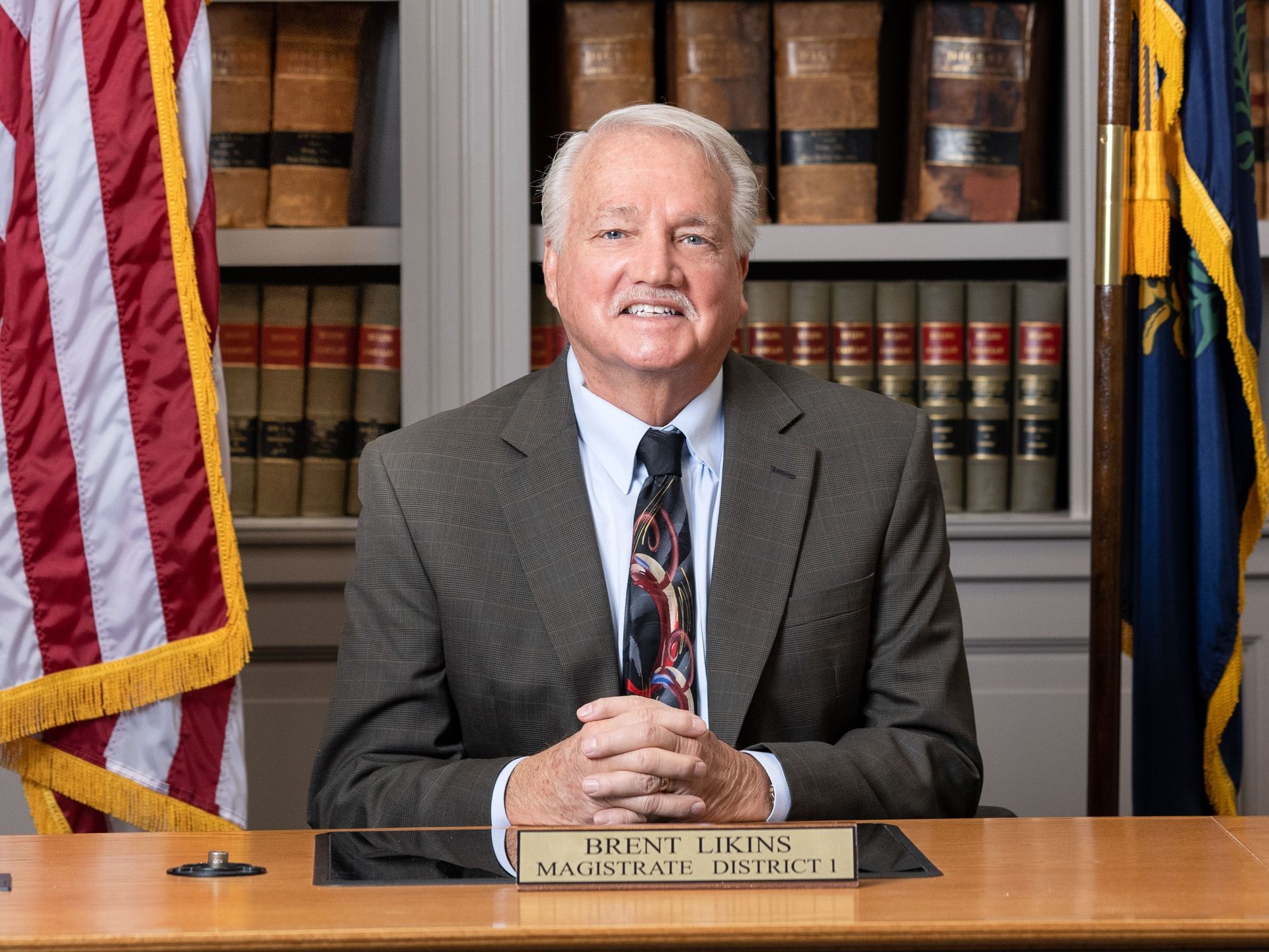 A man in a suit and tie is sitting at a desk with a name plate on it.