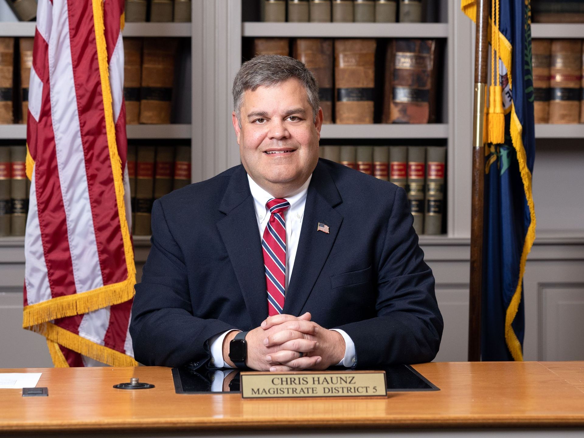 A man in a suit and tie is sitting at a desk in front of an american flag.