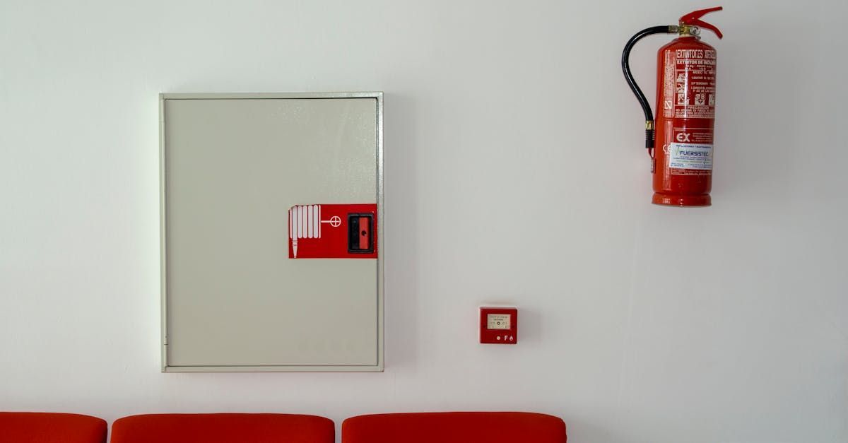 A fire extinguisher is hanging on a white wall next to a mirror.