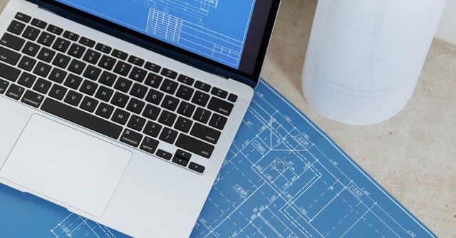 A laptop computer is sitting on top of a blueprint.