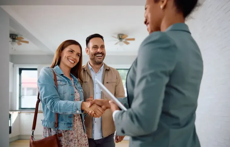 Smiling couple shaking hands with a realtor in a bright living room during a home viewing