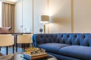 Modern living room with a navy tufted sofa, blue chair, floor lamp, and chess set on a glass coffee table