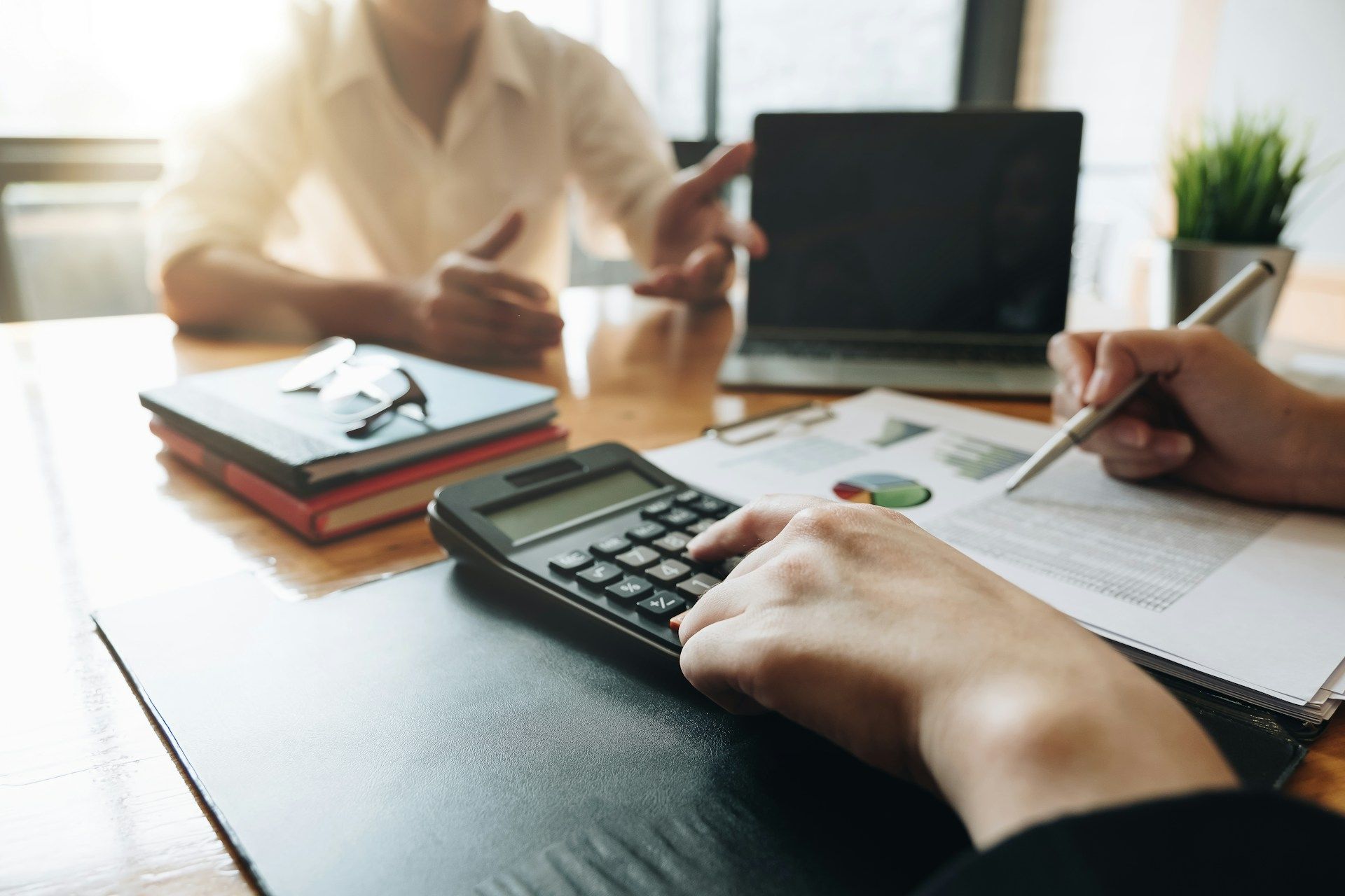 Two people at a desk, reviewing paperwork. One person uses a calculator.