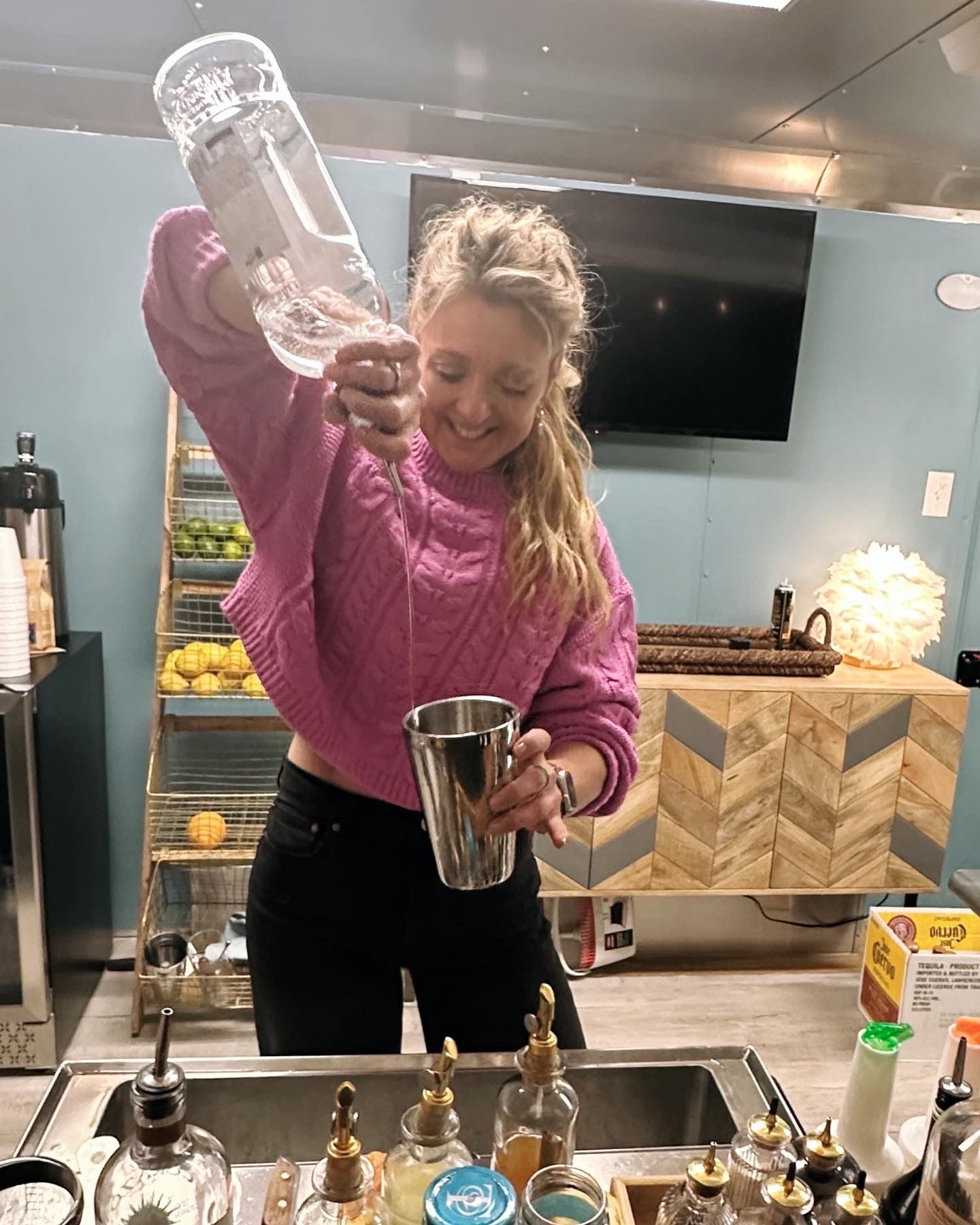 A woman in a pink sweater is pouring a drink into a bucket.