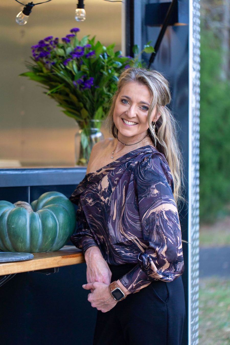 the owner is standing in front of a table with pumpkins and flowers .