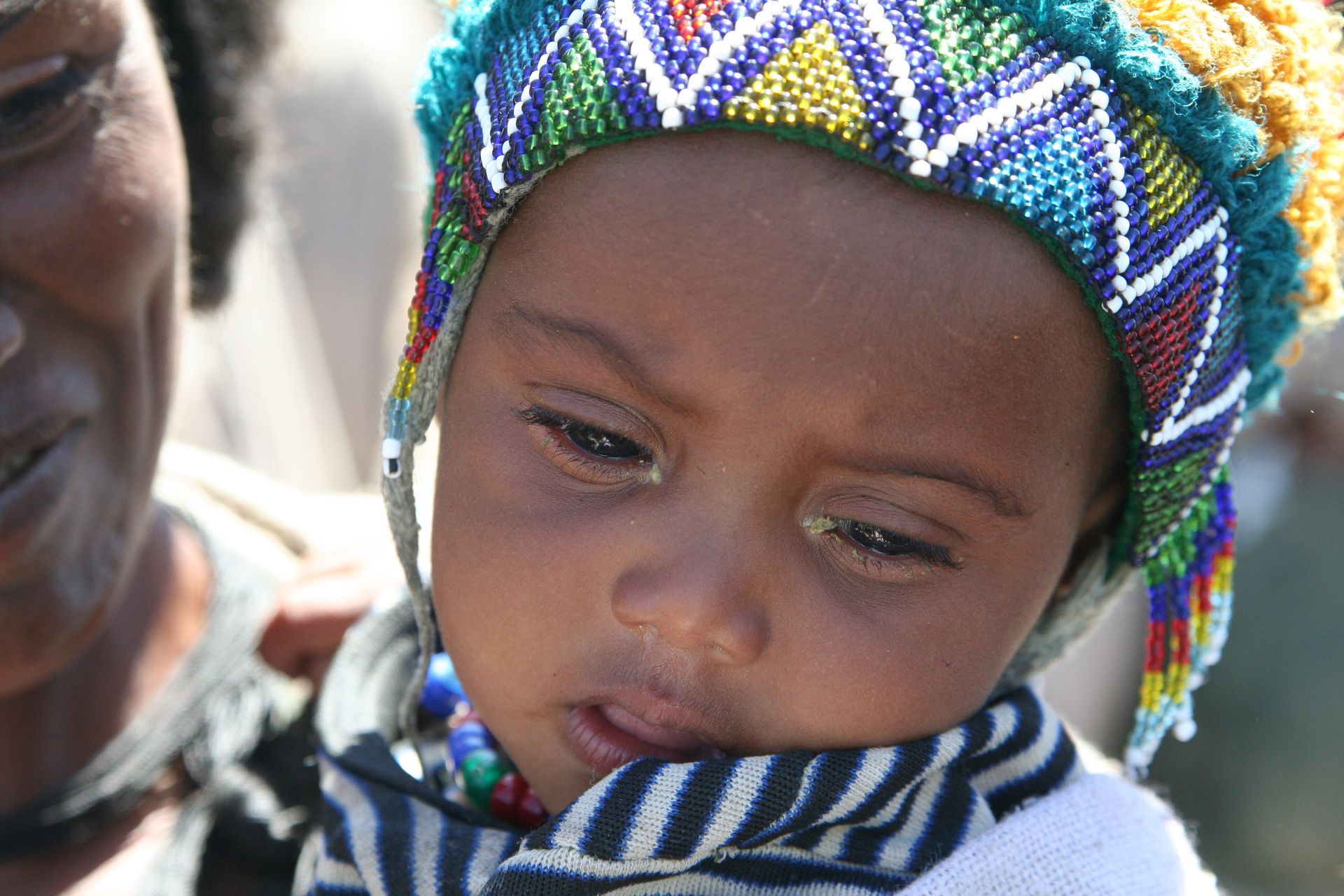 Ethiopian baby with colorful hat, held by a woman