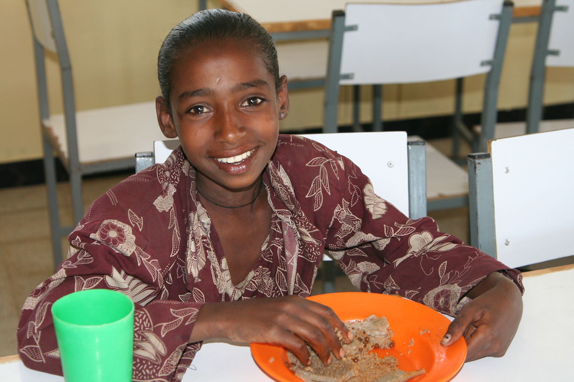 Ethiopian girl smiling while eating from an orange plate