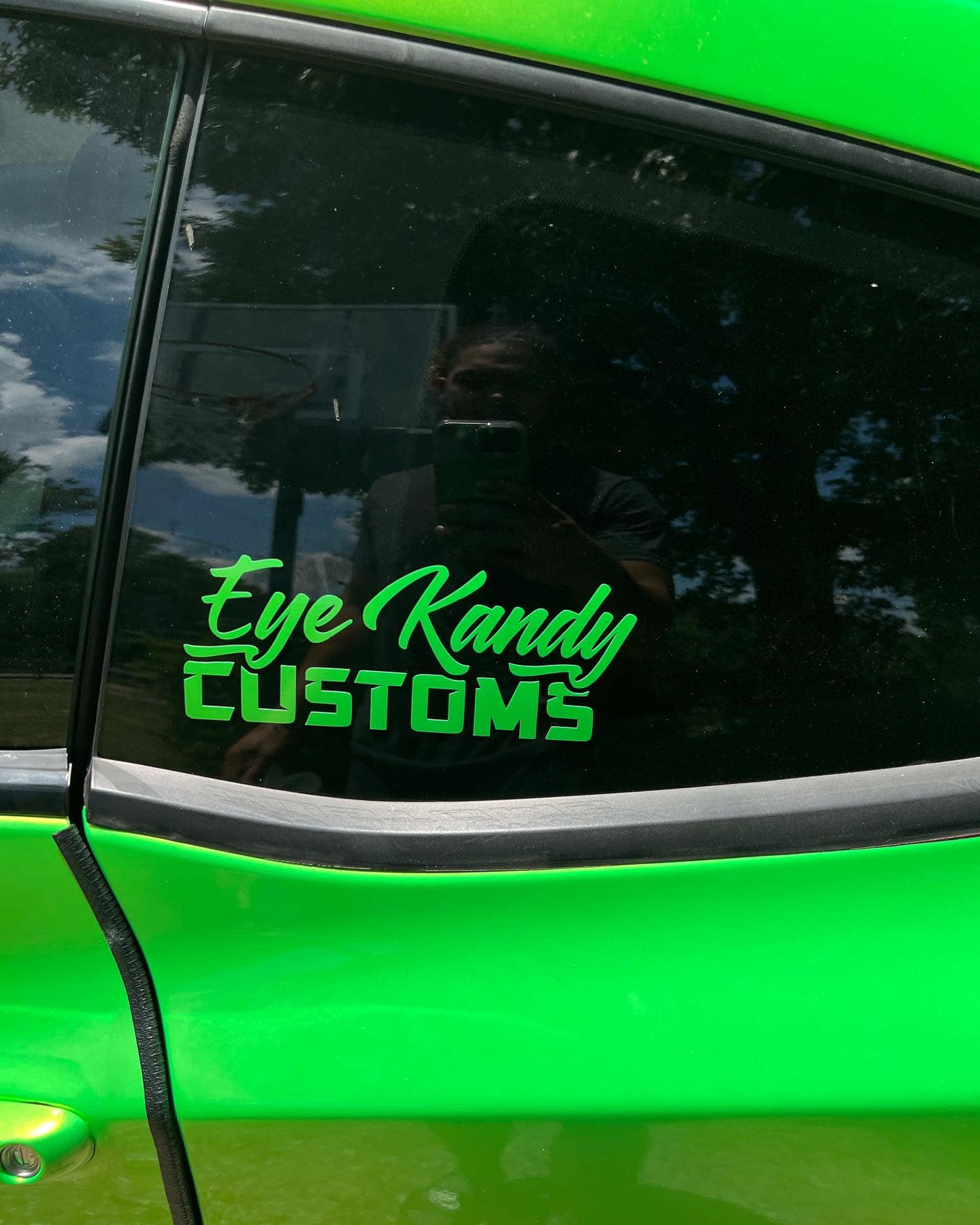 Close-up of a car with a vibrant green vinyl wrap featuring the Eye Kandy Customs logo on the window.