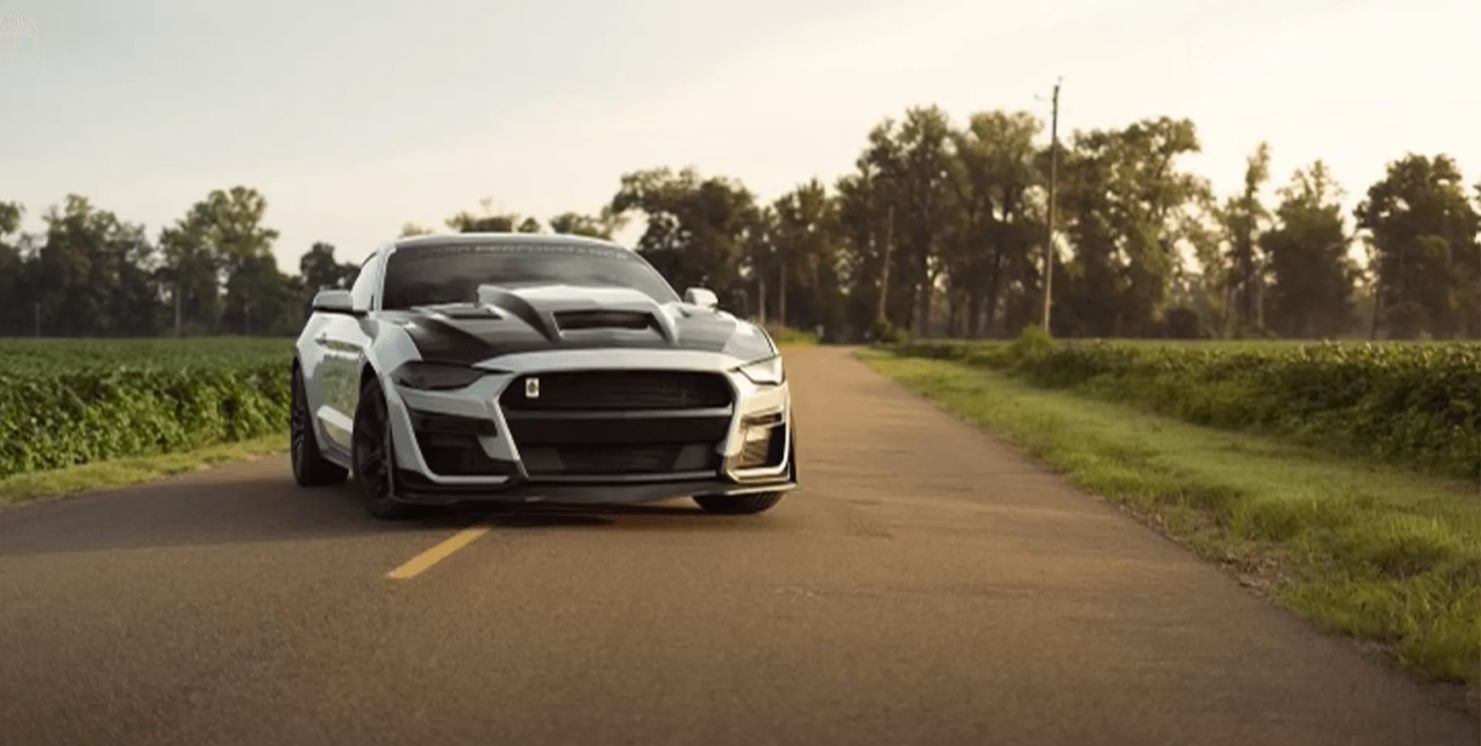 a white ford mustang is driving down a country road .