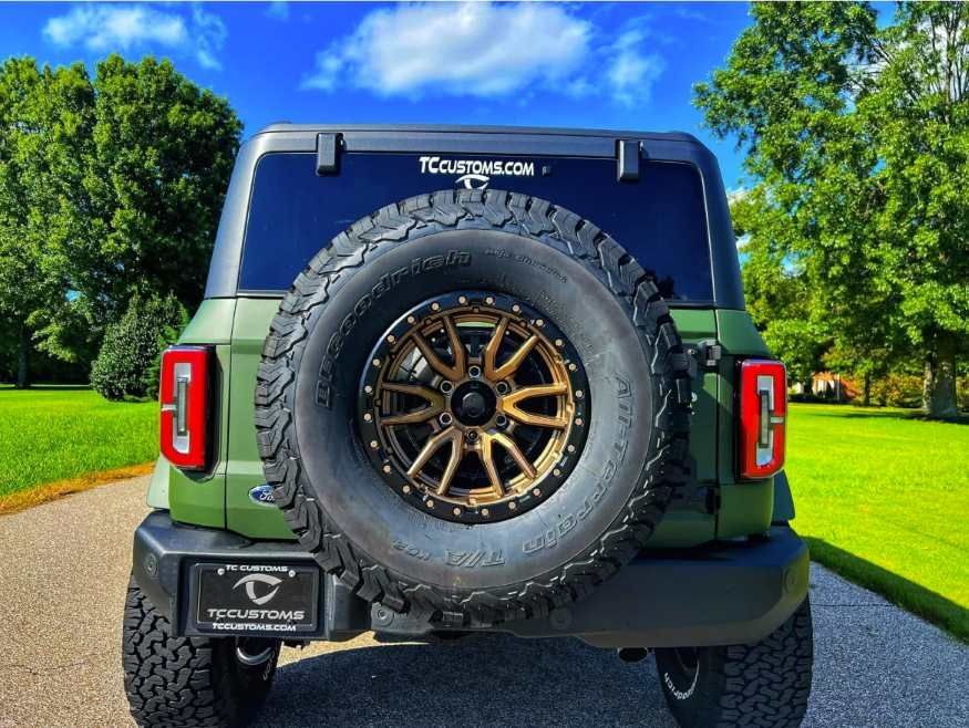 a green jeep with a spare tire is parked on the side of the road .