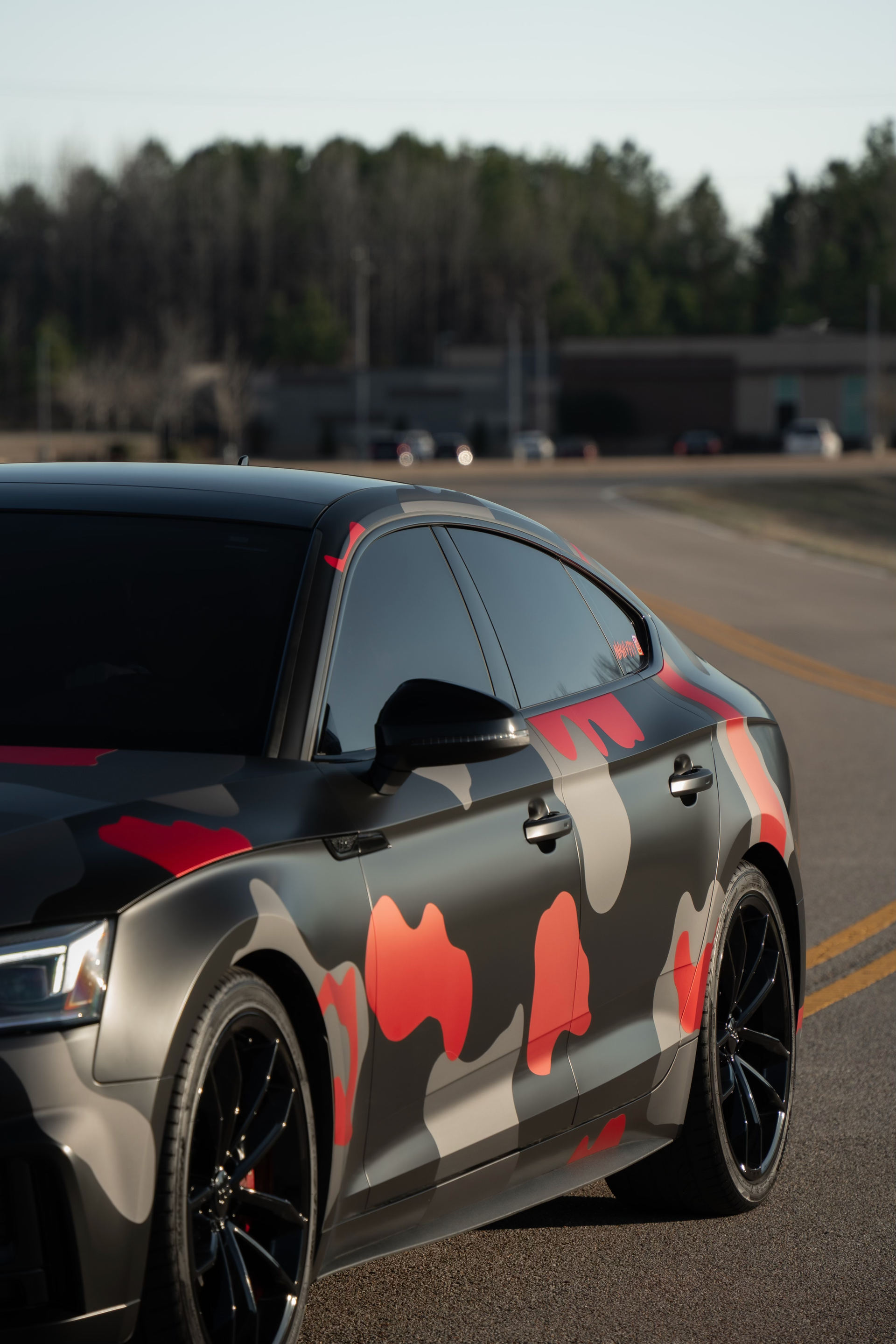 Custom car wrap featuring a camouflage pattern in black, grey, and red