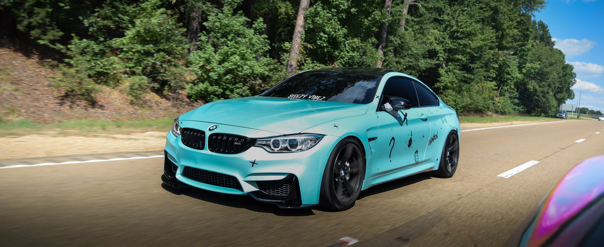 BMW M4 with a custom aquamarine wrap, driving down the road