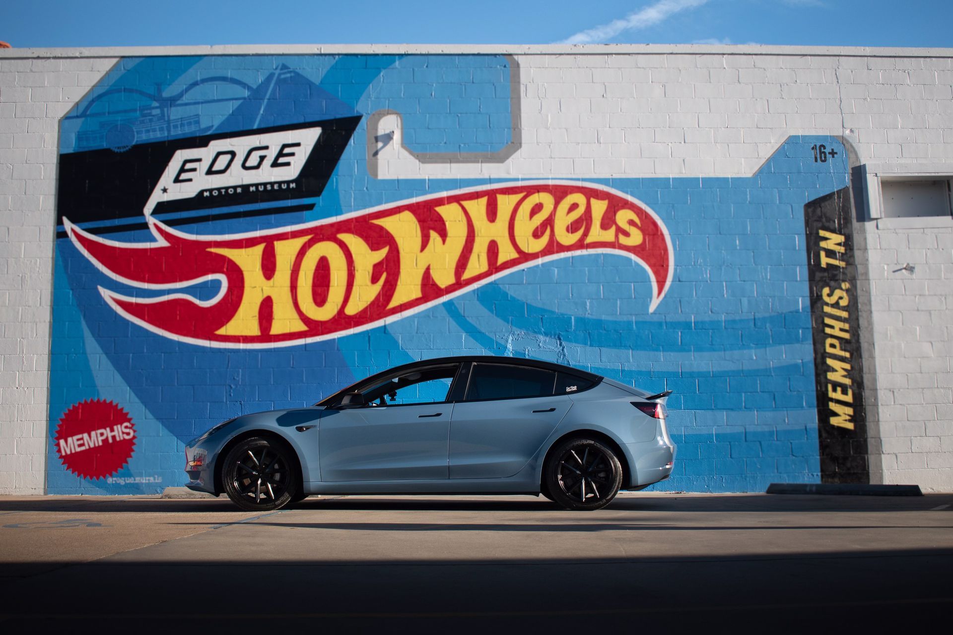Tesla Model 3 vinyl wrapped in Hot Wheels blue, parked in front of a Hot Wheels mural in Memphis TN