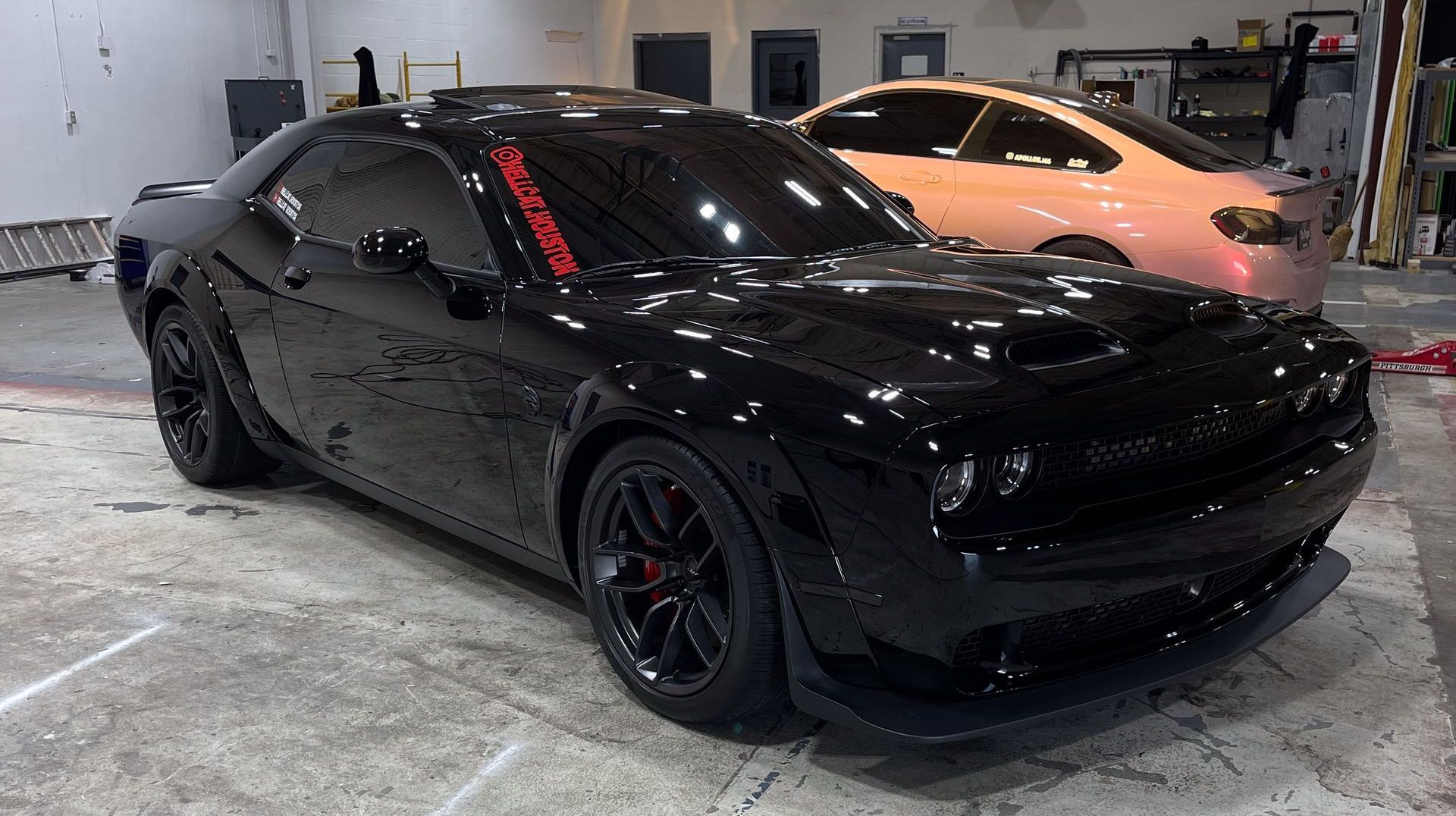 a black dodge challenger is parked in a garage next to a white car.