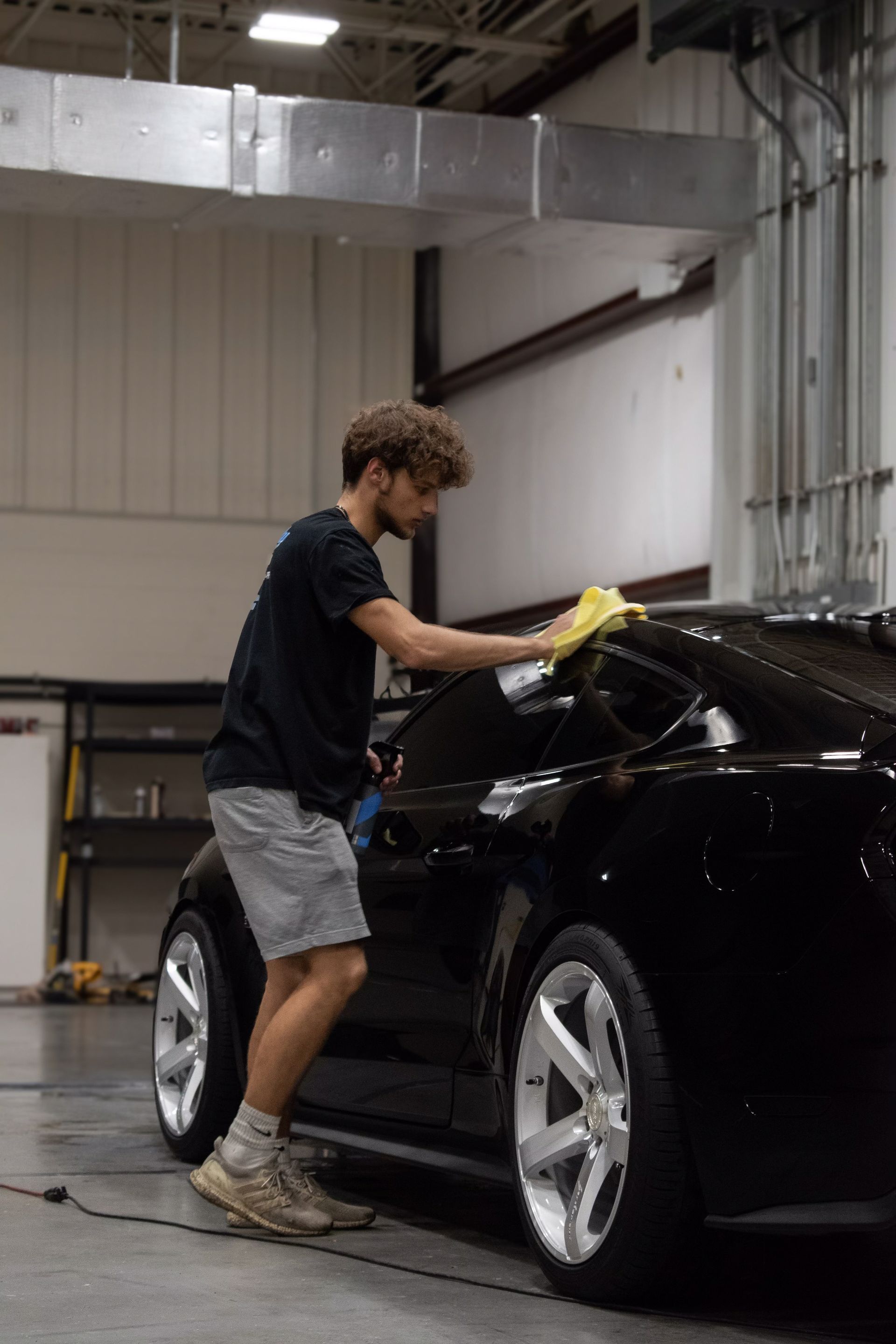 a man is polishing a black ford mustang in a garage.