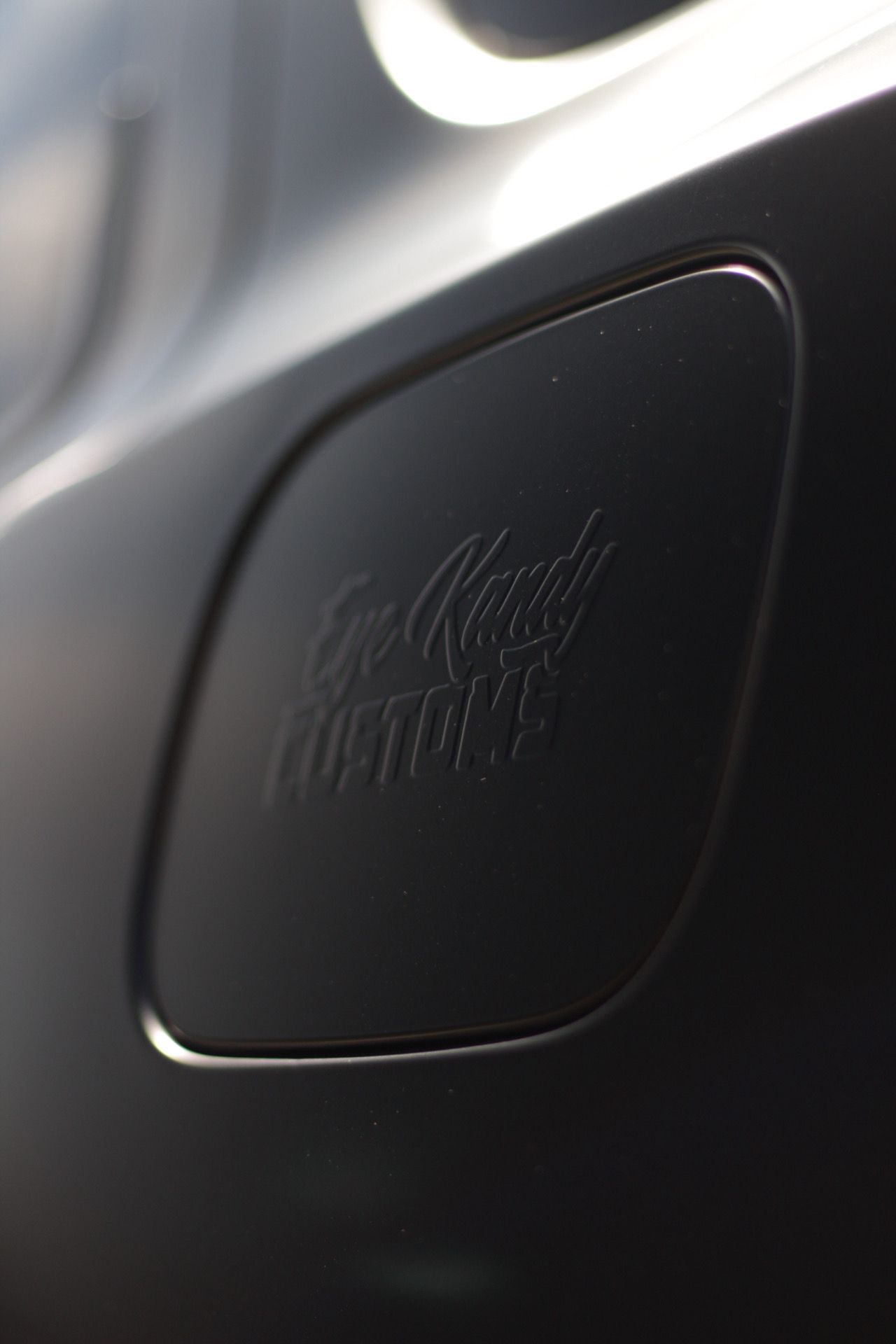 Close-up of a logo on the fuel door of a car, featuring the design of 'Eye Kandy Customs