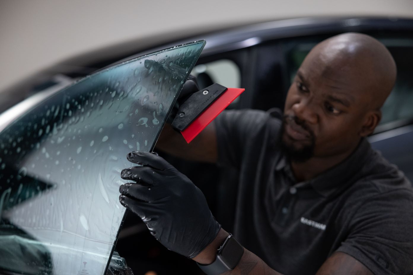 A man carefully applying window tint to a car window, smoothing out the film and ensuring a bubble-free finish.