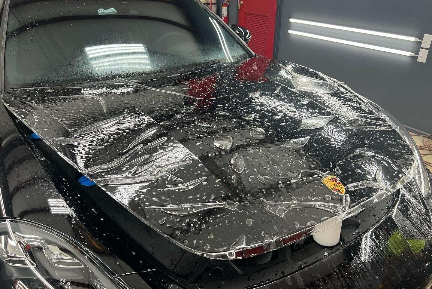 Close-up of a Porsche with clear paint protection film partially applied, showing the film in the installation process with visible creases and bubbles.