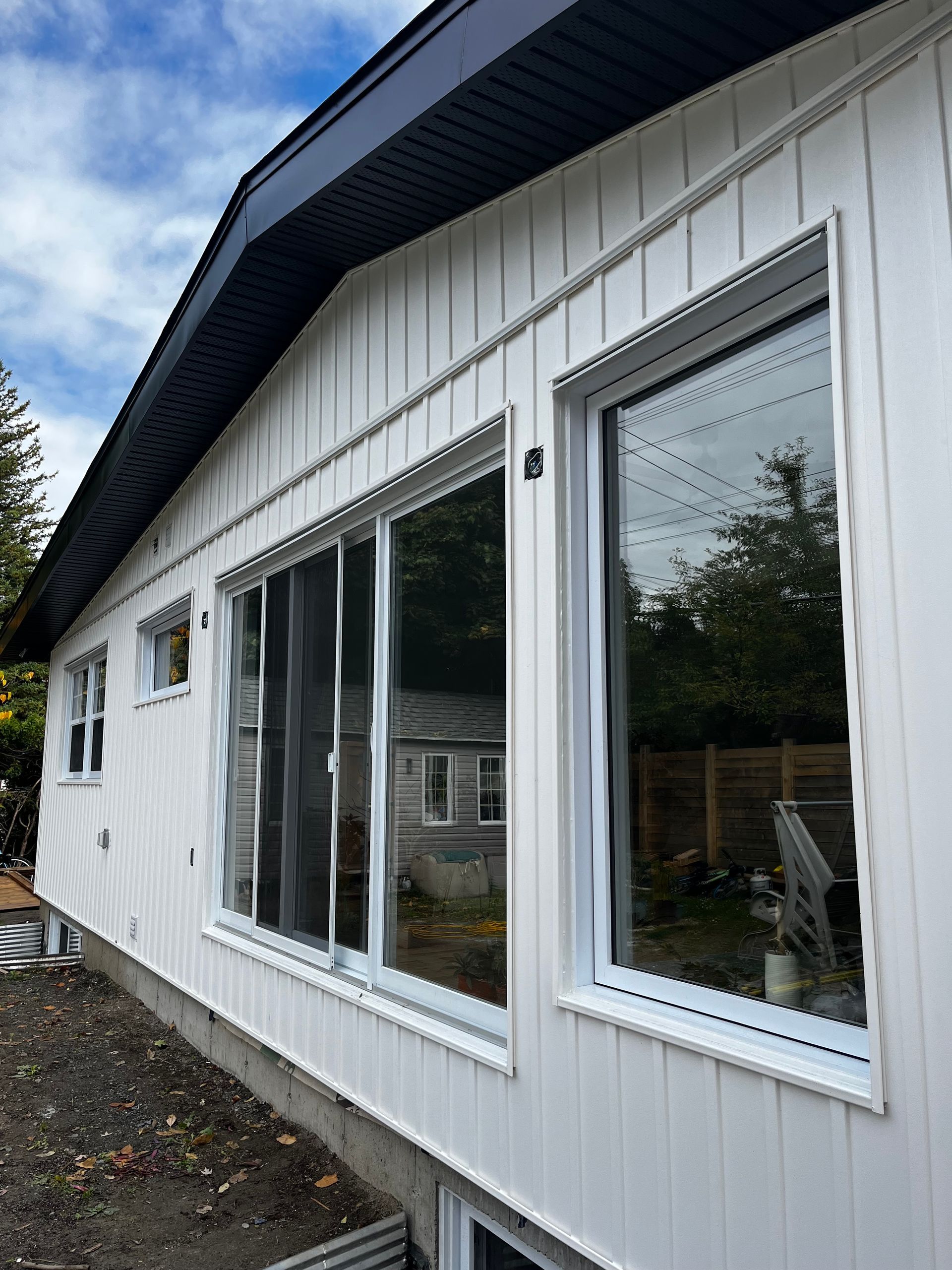 Bâtiment blanc aux grandes fenêtres et au toit sombre se détachant sur un ciel nuageux.