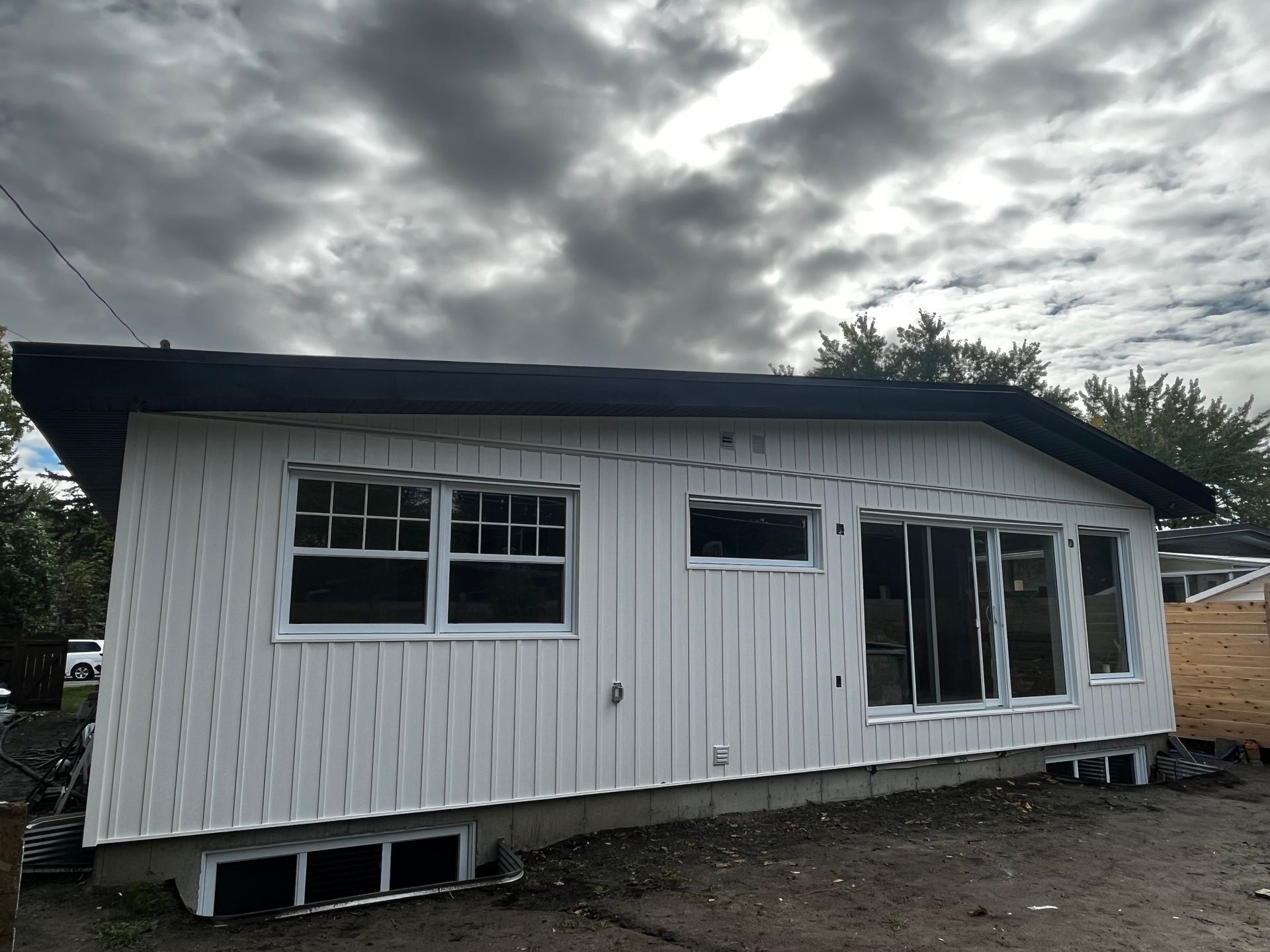 Bâtiment blanc avec toit et fenêtres noirs sur un ciel nuageux.